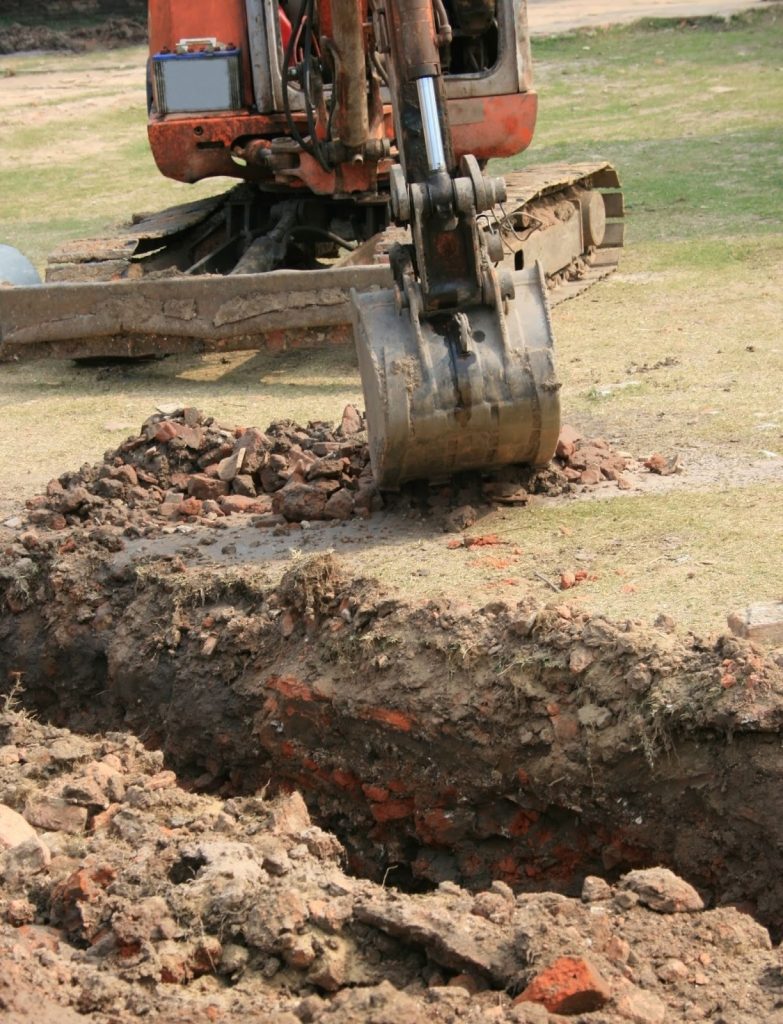 Backhoe digging a large trench, putting underground communication lines at risk.