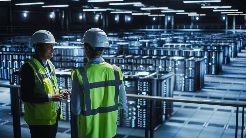 Two engineers plan a network modernization strategy from a platform overlooking racks of data center infrastructurea